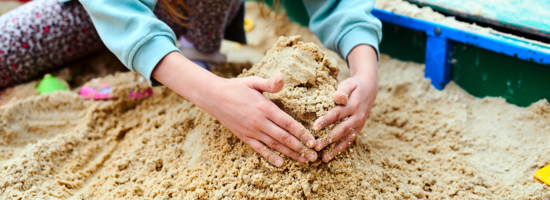 Volwassen handen spelen met zand in de zandbak.