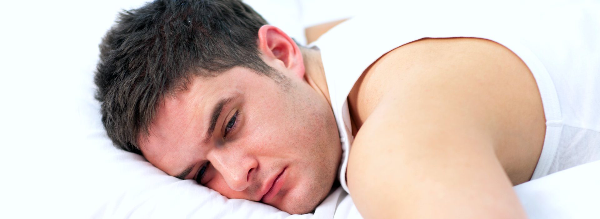 Man ligt op zijn zij in bed met open ogen. 
