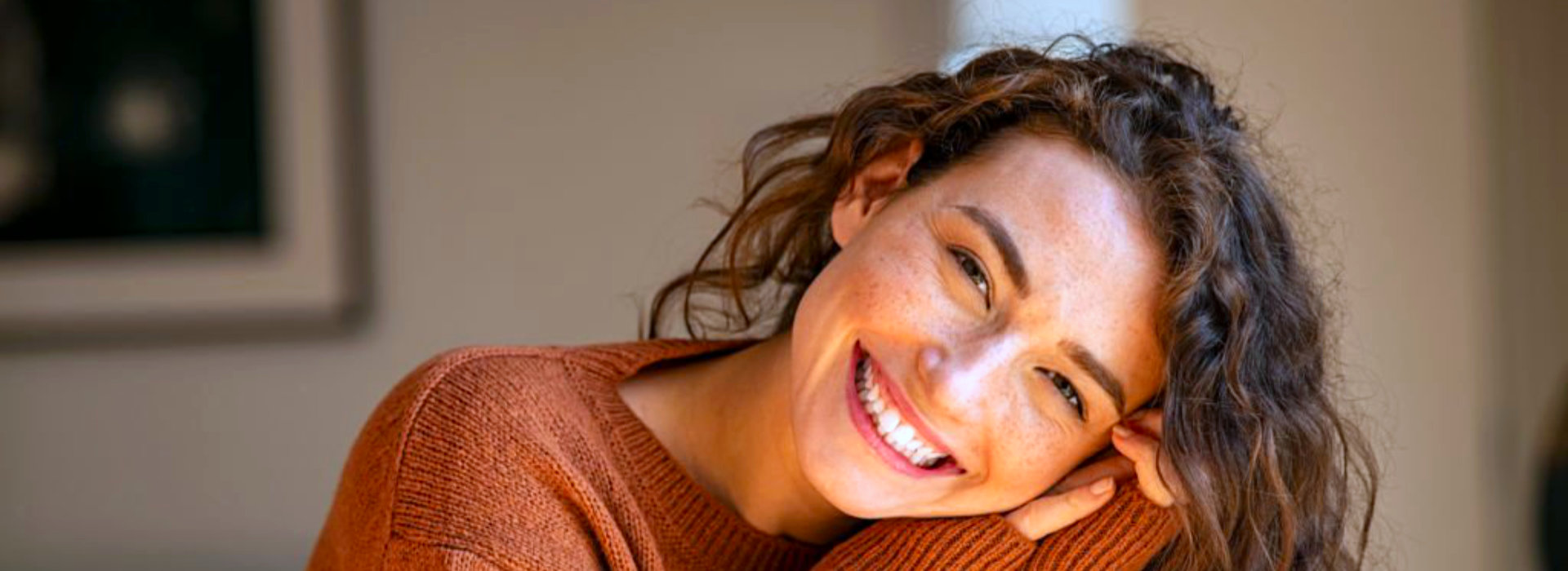 Vrolijke vrouw glimlacht warm en ontspannen, als topfoto bij het NieuwsBlog Gelukskunst op recept over de gedachte dat geluk en welbevinden te versterken zijn.