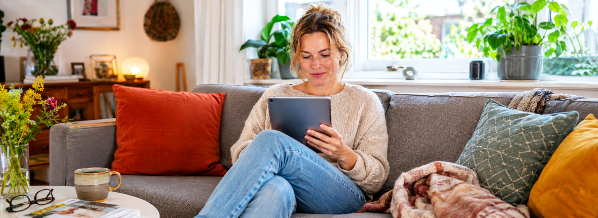 Vrouw leest op een tablet in een warme woonkamer, als beeld voor de NieuwsBlog met verhalen over leven, werk en coaching.