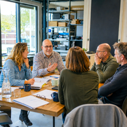 Coach begeleidt een organisatiecoaching gesprek met medewerkers rond een tafel
