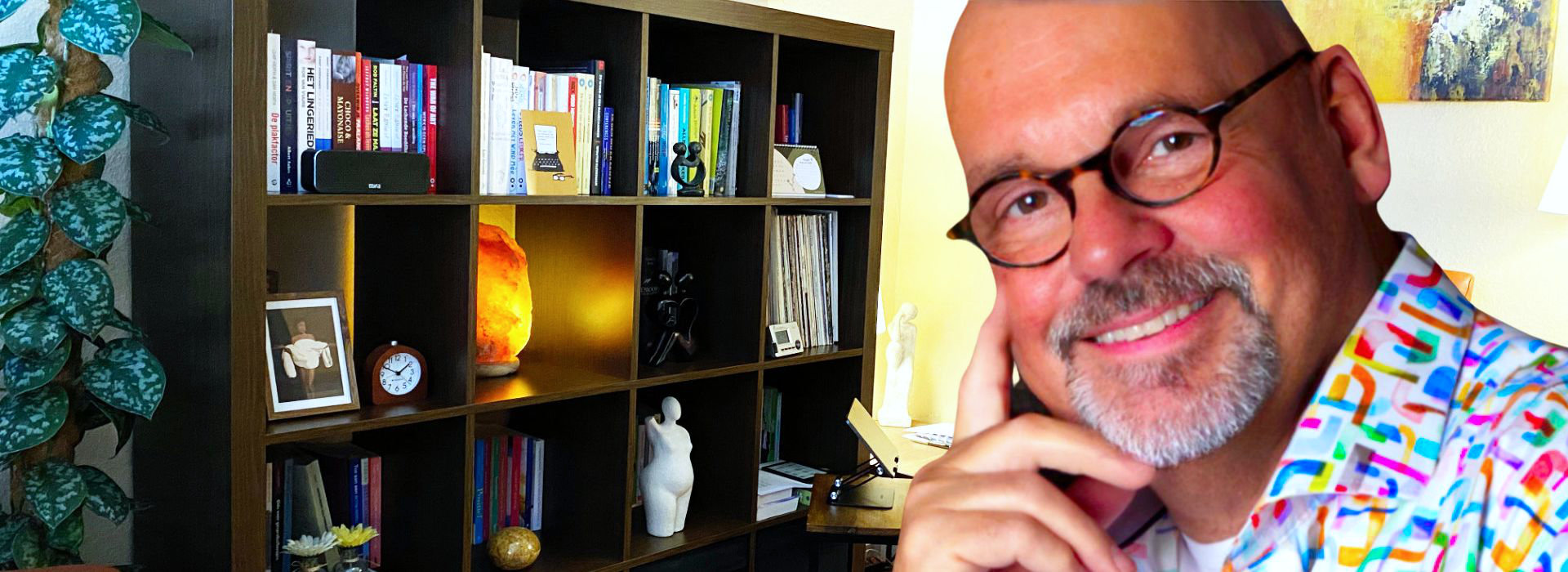 Freek zit glimlachend in zijn spreekkamer bij Spreek met Freek, met boekenkast en warme inrichting op de achtergrond.