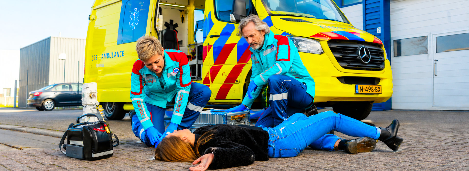 Ambulancemedewerkers helpen een vrouw op straat, als topfoto bij de WerkPrikkel Werkdruk 24/7.