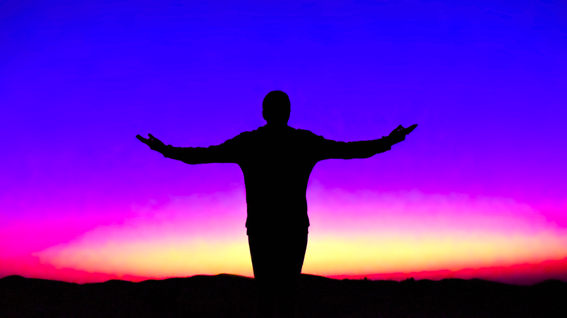 Silhouet van een man met open armen tegen een kleurrijke avondlucht, beeld bij opnieuw werkelijk waarnemen wat om je heen gebeurt.
