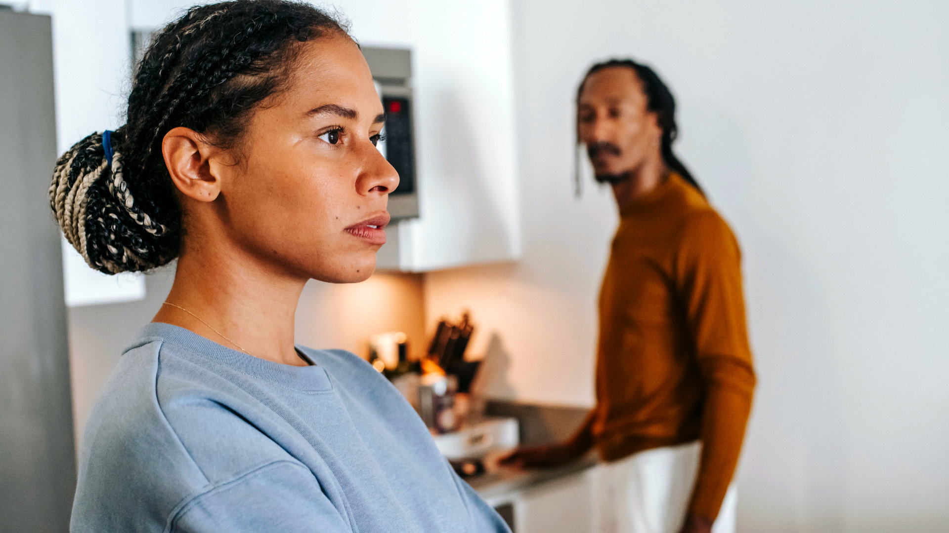 Vrouw kijkt gespannen voor zich uit terwijl een man vaag op de achtergrond staat, als beeld bij een NieuwsBlog over gaslighting, manipulatie en twijfel aan je eigen werkelijkheid.