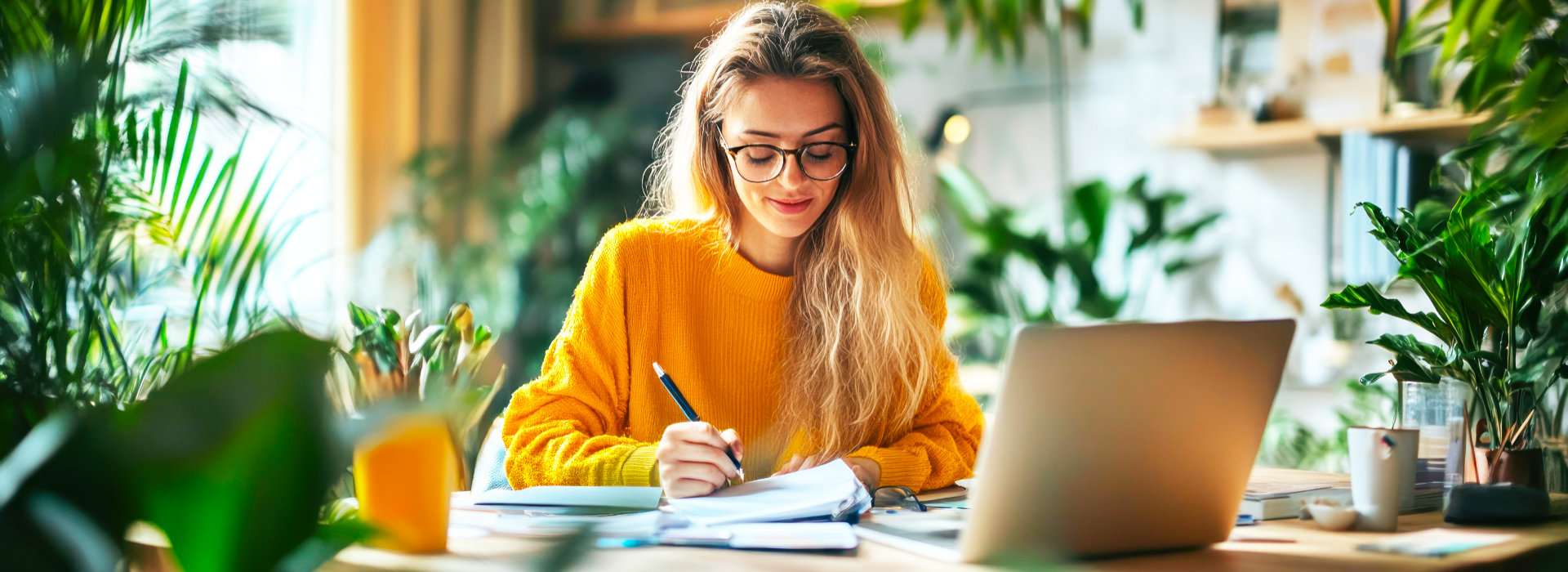 Vrouw schrijft thuis aantekeningen aan tafel naast haar laptop als beeld van persoonlijke online coaching.