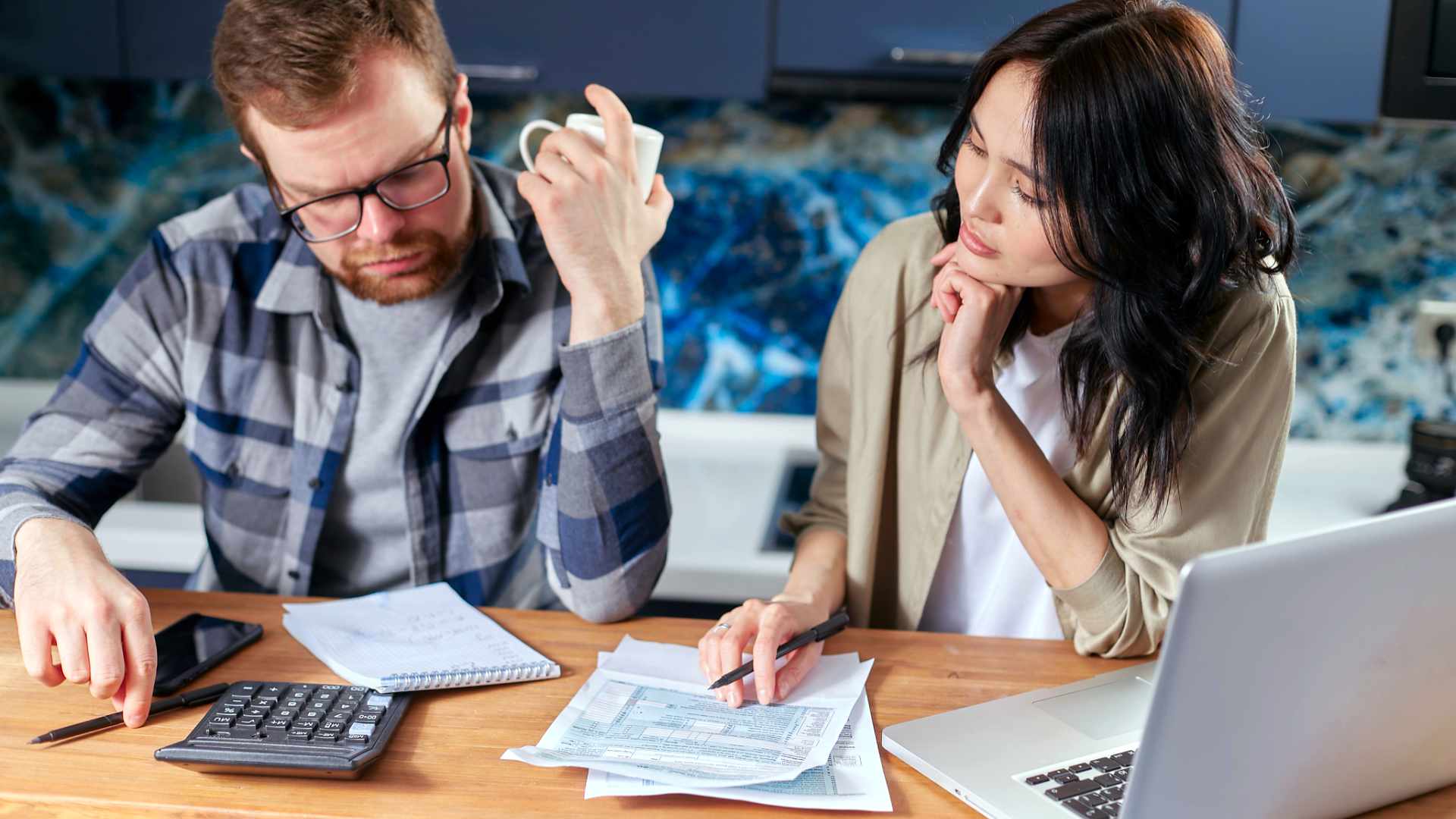 Man en vrouw bekijken samen rekeningen met rekenmachine en laptop, beeld bij financiële stress, overheidsregelingen en bestaanszekerheid.