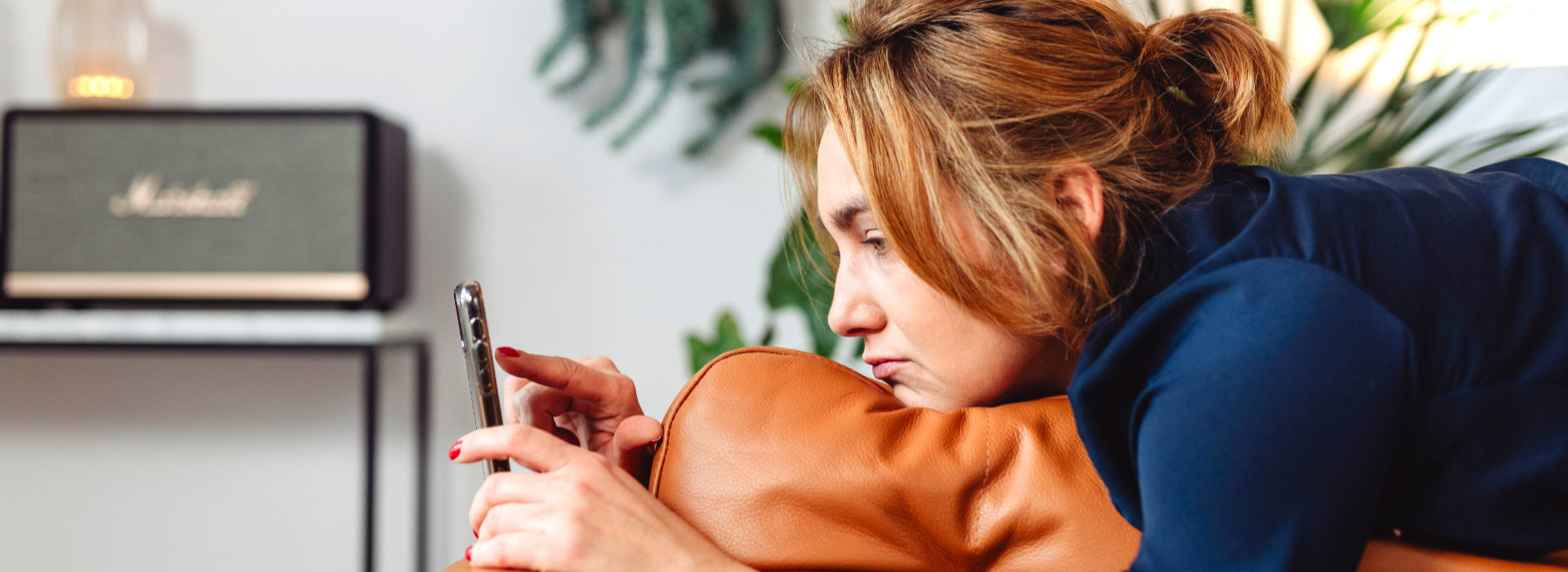 Vrouw ligt op de bank terwijl haar aandacht bij haar smartphone blijft, beeld bij coaching rond de pauzeknop indrukken, rust en herstel bij Spreek met Freek.