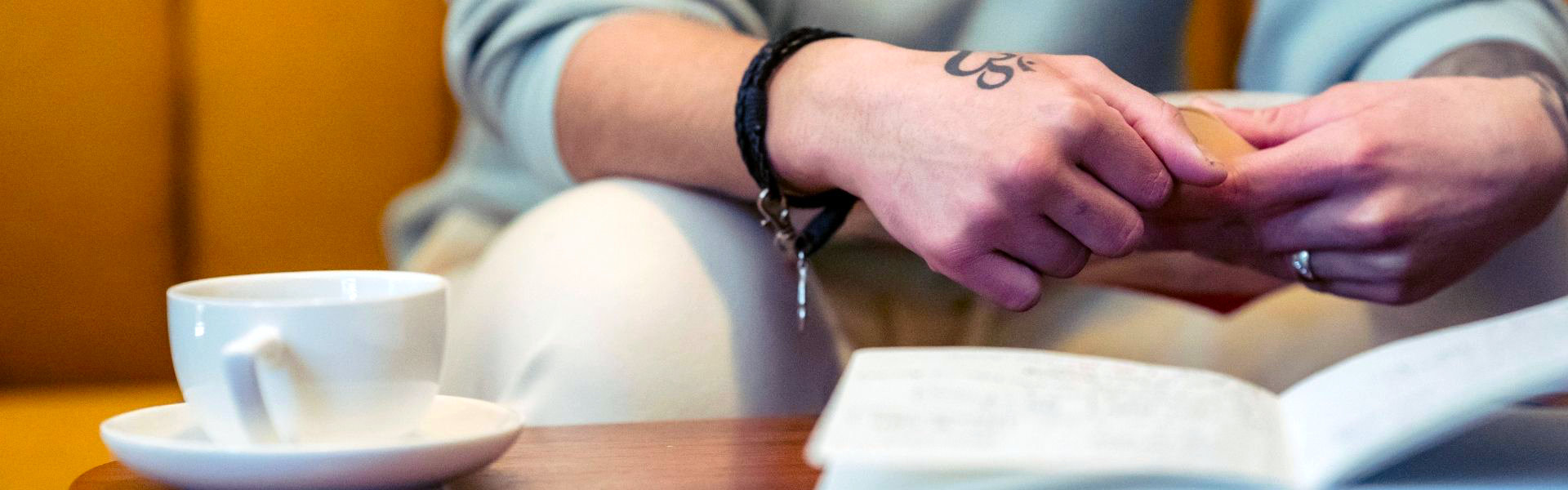 Persoon houdt de handen in elkaar naast een open notitieboek, beeld bij coaching rond onzekerheid, zelftwijfel en jezelf inhouden bij Spreek met Freek.