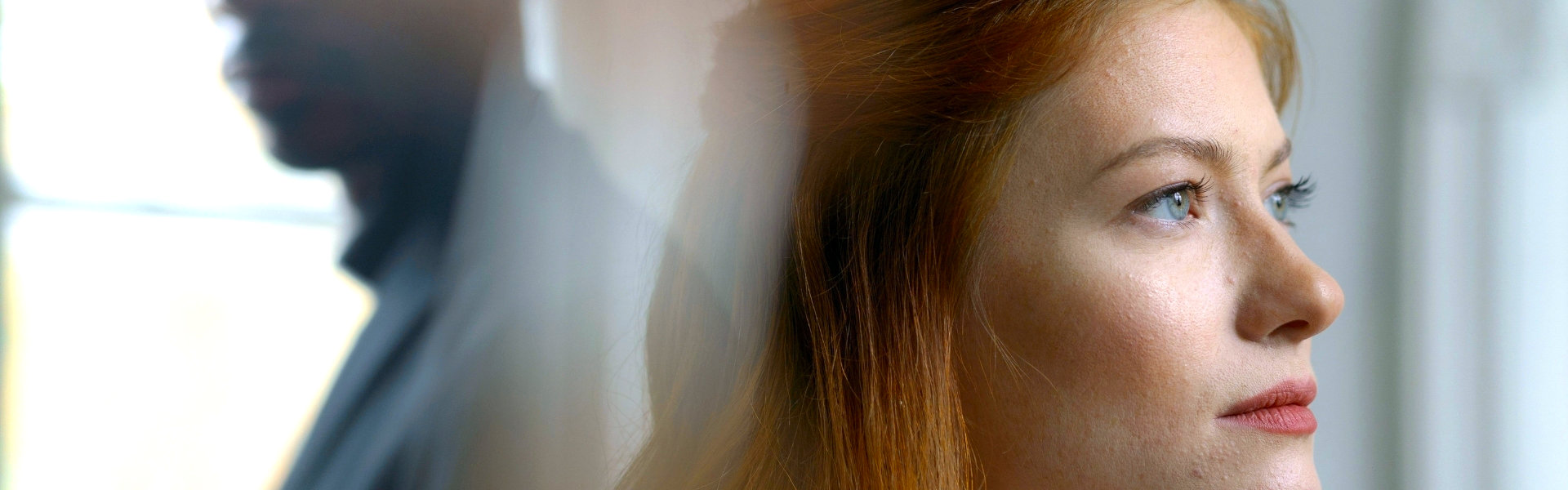 Vrouw kijkt weg terwijl haar partner vaag op de achtergrond zichtbaar is, beeld bij relatietherapie rond emotionele afstand en verbinding bij Spreek met Freek.
