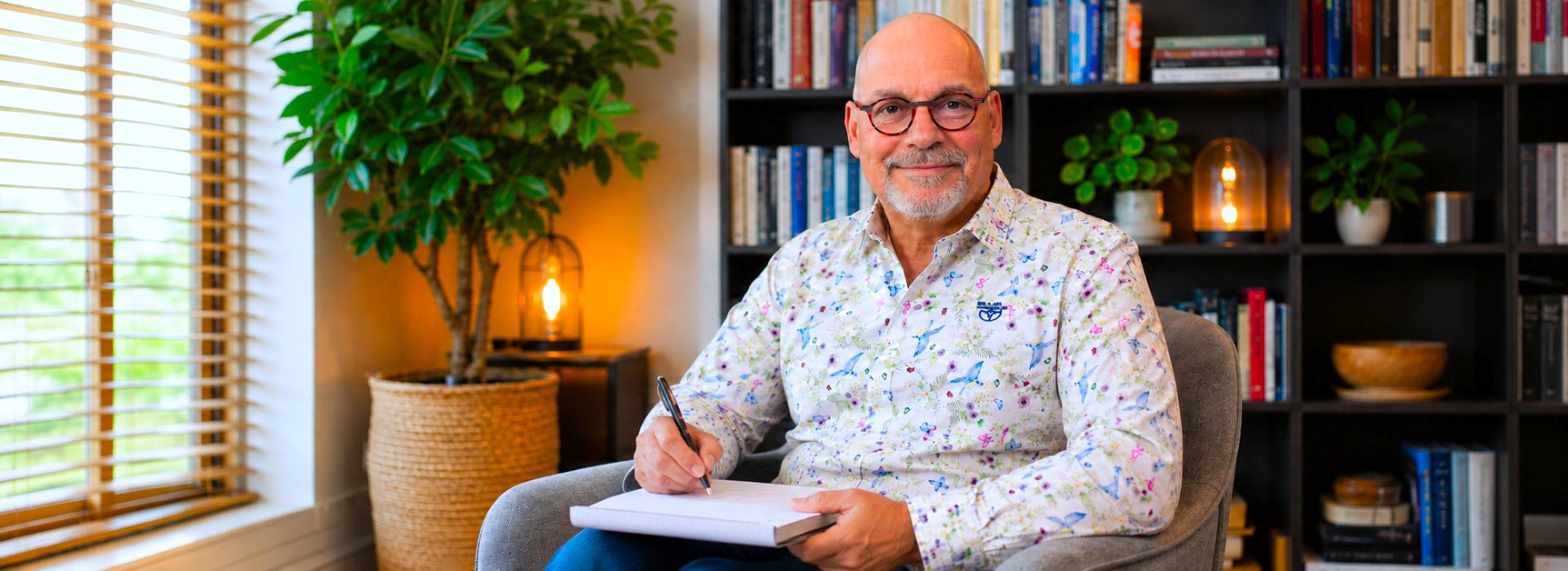 Coach van Spreek met Freek zit met pen en notitieblok in een warme spreekkamer, als beeld bij coaching en psychologie.